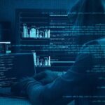 Hacker in a hoodie at a multi-monitor setup displaying code and graphs, blue-toned lighting.