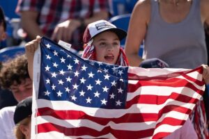 Young girl in a cap holding up a large American flag at a stadium event