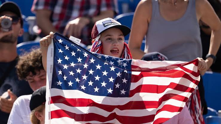 Young girl in a cap holding up a large American flag at a stadium event