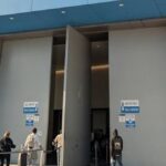 Entrance to San Ysidro Land Port of Entry, east pedestrian side, with people queued outside and a U.S. flag nearby