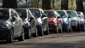 Row of parked cars in different colors along a tree-lined street.