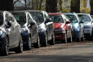 Row of parked cars in different colors along a tree-lined street.