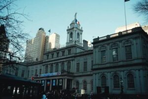Historic city hall building with clock tower and flagpoles, daytime, with people at the entrance