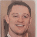 Head-and-shoulders portrait of a smiling man with short dark hair in a suit