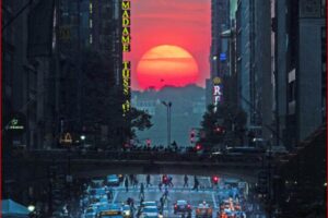 Sunset over a busy city street with a crowd crossing beneath an overpass and neon signs on the buildings side.
