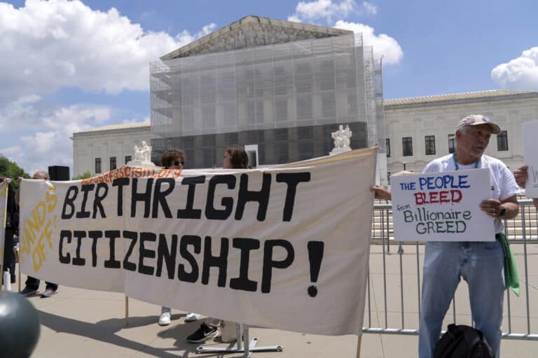 Protesters hold a large banner reading 'BIRTHRIGHT CITIZENSHIP' in front of a government building under a blue sky.