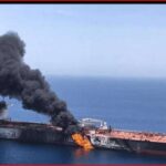 Two men flank a burning ship at sea with thick black smoke rising between them.