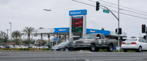 Walmart gas station with price board and multiple cars at a street intersection under cloudy skies