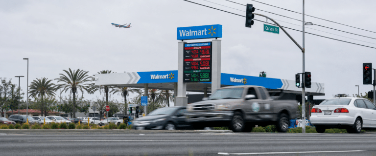 Walmart gas station with price board and multiple cars at a street intersection under cloudy skies
