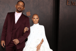 Will Smith and Jada Pinkett Smith pose arm-in-arm on a dark backdrop at an Emancipation premiere in formal attire (burgundy suit and white gown).