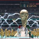 World Cup trophy on a pedestal surrounded by gold-clad performers in a stadium with fireworks and cheering crowds