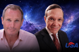 Two men pose together against a starry space backdrop with the USA Herald logo in the bottom right corner.