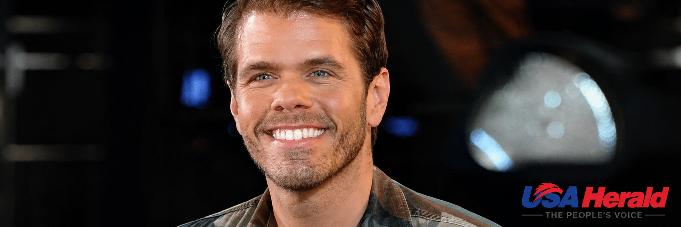 Close-up portrait of a smiling man in a plaid shirt, dark background, with the USA Herald logo in the lower right corner.