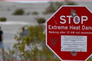 Red stop sign with text 'STOP Extreme Heat Danger' and 'Walking after 10 AM not recommended'; blurred figures walking in a desert landscape in the background.