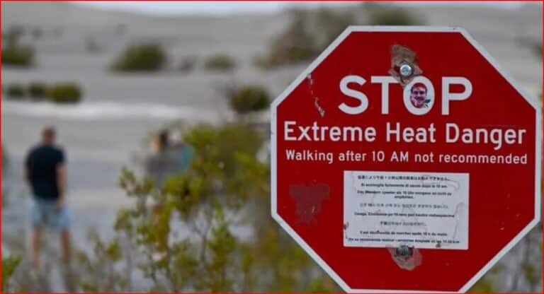 Red stop sign with text 'STOP Extreme Heat Danger' and 'Walking after 10 AM not recommended'; blurred figures walking in a desert landscape in the background.