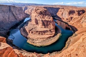 Aerial view of red canyon walls with a blue-green river looping around a central sandstone promontory in a horseshoe bend.