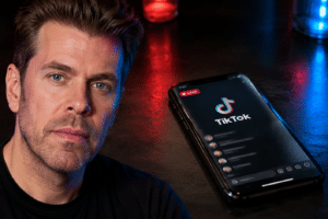 Editorial composite of Perez Hilton beside a smartphone displaying TikTok Live as emergency lights reflect in the background.