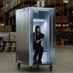 Warehouse worker sits inside a tall metal cabinet on wheels with the door open.