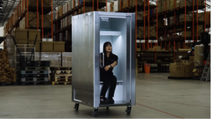 Warehouse worker sits inside a tall metal cabinet on wheels with the door open.