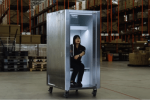 Warehouse worker sits inside a tall metal cabinet on wheels with the door open.
