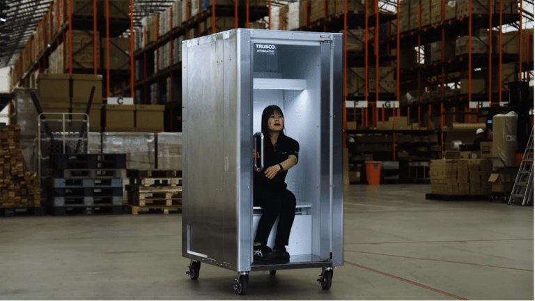 Warehouse worker sits inside a tall metal cabinet on wheels with the door open.