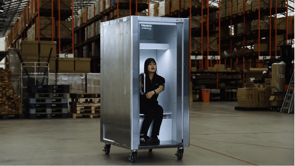 Warehouse worker sits inside a tall metal cabinet on wheels with the door open.