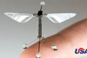Close-up of a tiny winged micro-drone balanced on a fingertip, with silver foil wings.