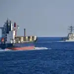 A U.S. Navy destroyer escorts a merchant vessel through the Strait of Hormuz.
