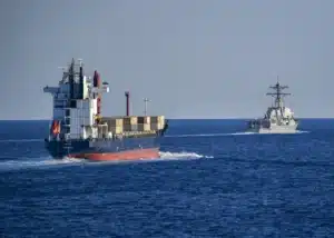 A U.S. Navy destroyer escorts a merchant vessel through the Strait of Hormuz.