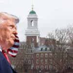 Man in a dark suit and red tie seen in profile, with an American flag behind him and a brick campus building with a green-domed tower in the background.