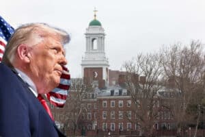 Man in a dark suit and red tie seen in profile, with an American flag behind him and a brick campus building with a green-domed tower in the background.