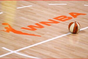 Basketball rests on a polished wooden court beside an orange WINBA logo and white lines on the floor.