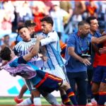 Soccer players and staff involved in a scuffle on the field, grabbing and pushing near the goal area of a match in progress.