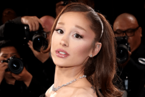 Woman wearing a diamond necklace posing on a red carpet, photographers in the background.