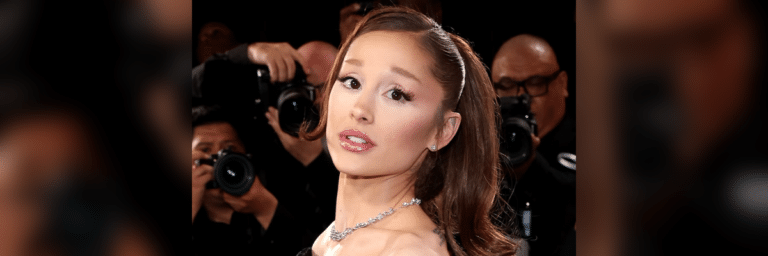 Woman wearing a diamond necklace posing on a red carpet, photographers in the background.