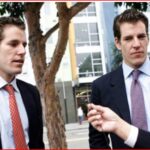 Two suited men on a city street being interviewed, a microphone held toward them by a person off-camera