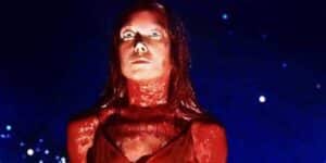 Woman with red lighting on face and neck, wide-eyed expression, looking upward against a dark blue, speckled background.