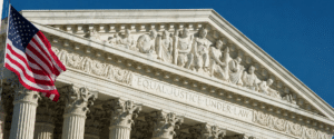 US Supreme Court building façade with sculpted frieze and the inscription 'EQUAL JUSTICE UNDER LAW' beside a waving American flag