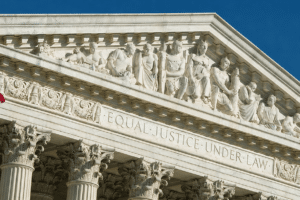 US Supreme Court building façade with sculpted frieze and the inscription 'EQUAL JUSTICE UNDER LAW' beside a waving American flag