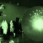 C-130 military transport on the tarmac at night with crew loading under green night-vision lighting