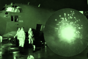 C-130 military transport on the tarmac at night with crew loading under green night-vision lighting