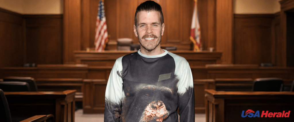 Smiling man stands in a courtroom with wooden panels and a flag behind him.