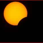Partial solar eclipse: a bright orange sun partially obscured by the moon against a dark sky.