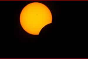 Partial solar eclipse: a bright orange sun partially obscured by the moon against a dark sky.