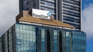 Steadfast sign on a modern glass office building with a tan roof, a tall dark high-rise behind it.