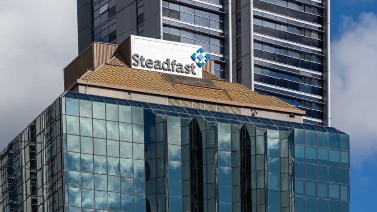 Steadfast sign on a modern glass office building with a tan roof, a tall dark high-rise behind it.