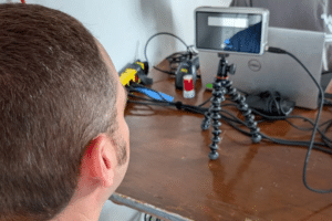 Back of a man’s head at a desk, smartphone on a small tripod among cables and tech gear.