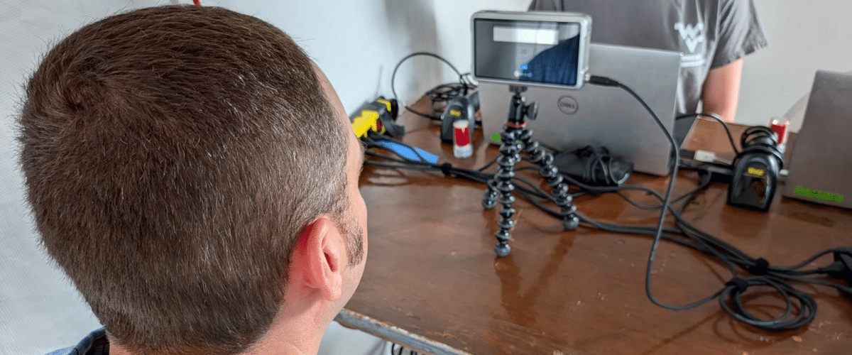 Back of a man’s head at a desk, smartphone on a small tripod among cables and tech gear.
