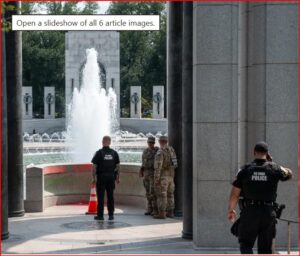 Uniformed police officers stand near a fountain at a memorial, with tall stone pillars surrounding.