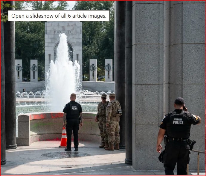 Uniformed police officers stand near a fountain at a memorial, with tall stone pillars surrounding.